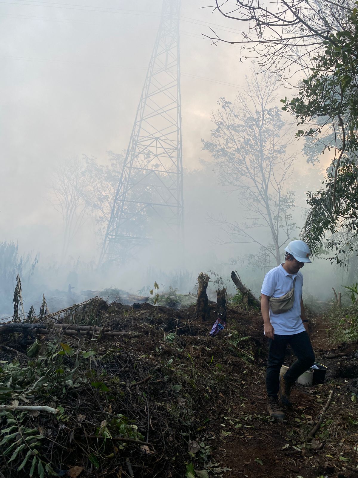 DIKEPUNG ASAP: Petugas PLN saat mengecek kondisi tower transmisi yang sempat dikepung api hingga berasap disekitarnya, Senin (5/8/2024). (foto: PLN)